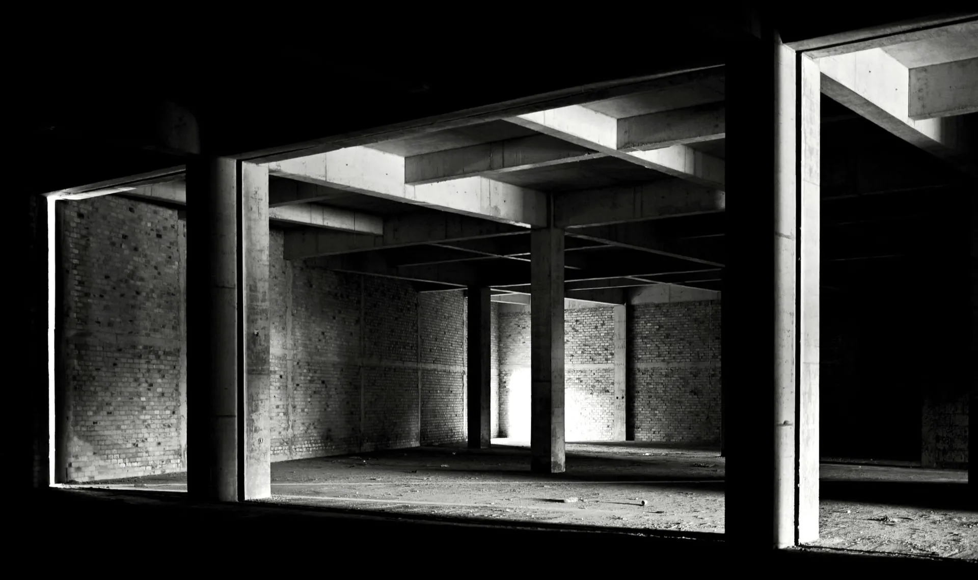 Black and white view of an empty industrial interior with concrete columns and brick walls