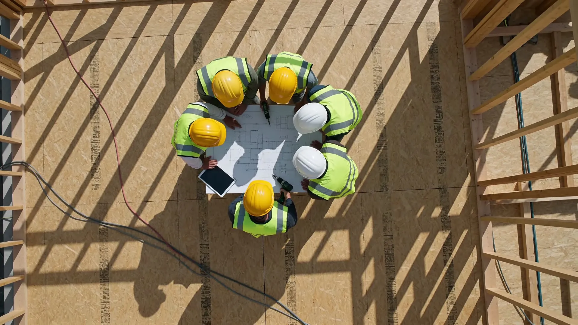 Overhead view of a crew gathered around drawings on a deck